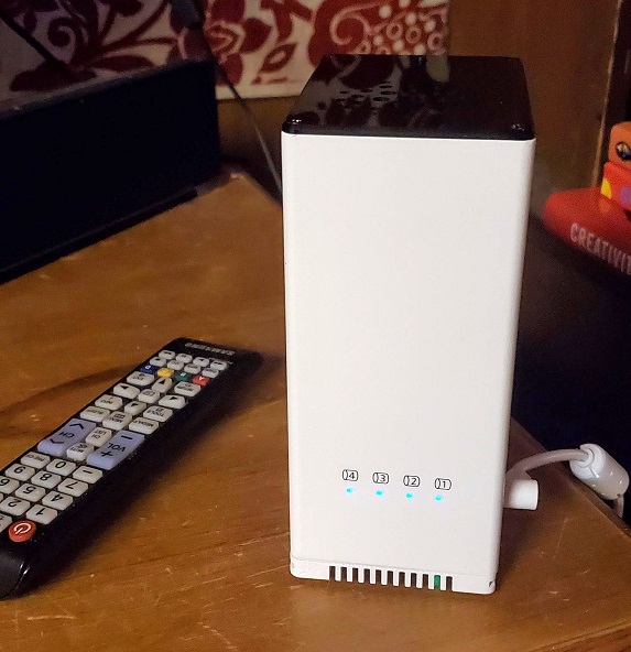 a very small computer tower on a wooden surface next to a TV remote for size comparison